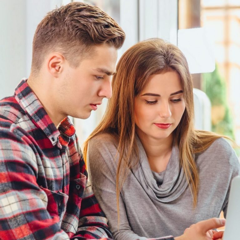 A young man and woman sitting together, intently looking at a smartphone.